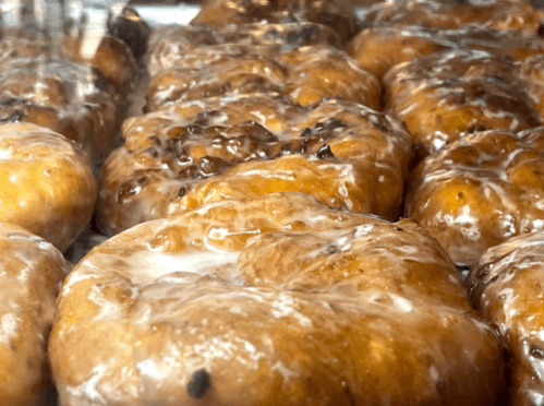 Close-up of glazed donuts with a shiny, sticky surface and chocolate chips, displayed in a glass case.