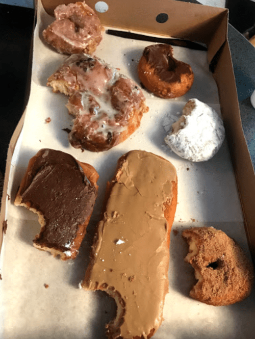 A box of assorted donuts, including glazed, chocolate-covered, and powdered varieties, some partially eaten.