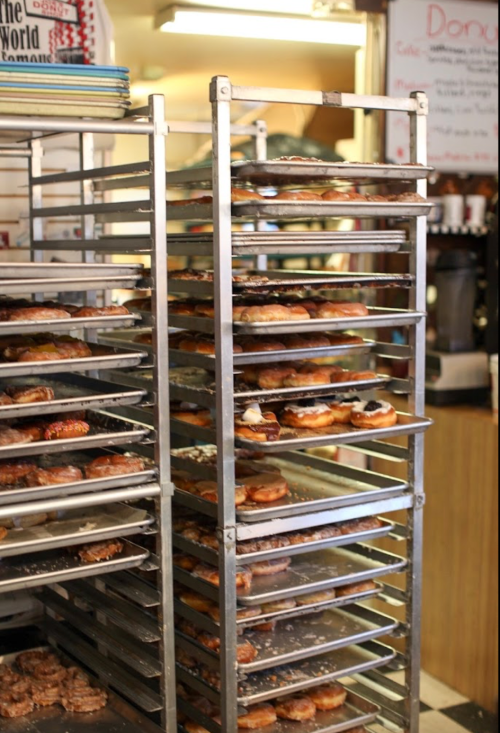A metal rack filled with various donuts, showcasing a variety of toppings and flavors in a bakery setting.