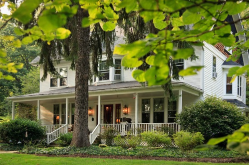 A charming white house with a porch, surrounded by lush greenery and trees in a serene setting.