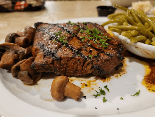 Grilled steak with mushrooms and green beans on a white plate, garnished with parsley.