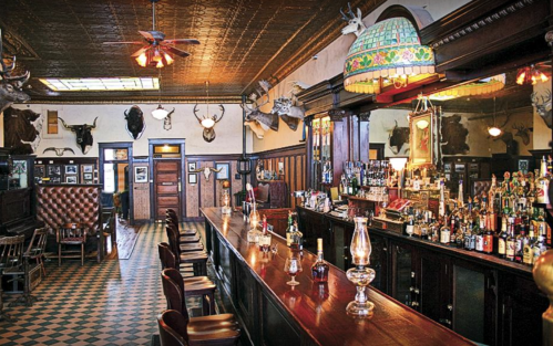 A vintage bar interior with a long wooden counter, shelves of liquor, and decorative taxidermy on the walls.