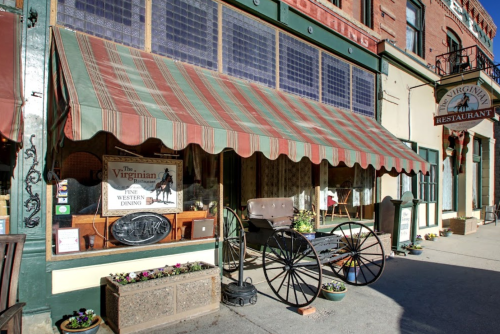 Exterior of The Virginian restaurant featuring a striped awning, a horse-drawn carriage, and flower planters.