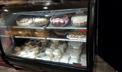 A display case filled with various cakes and desserts, including layered cakes and individual servings in containers.