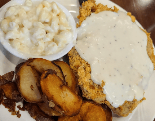 A plate featuring fried chicken with white gravy, seasoned potato wedges, and a side of creamy macaroni and cheese.