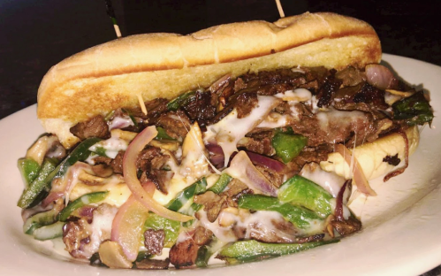 A loaded sandwich with grilled steak, peppers, onions, and melted cheese on a toasted hoagie roll.