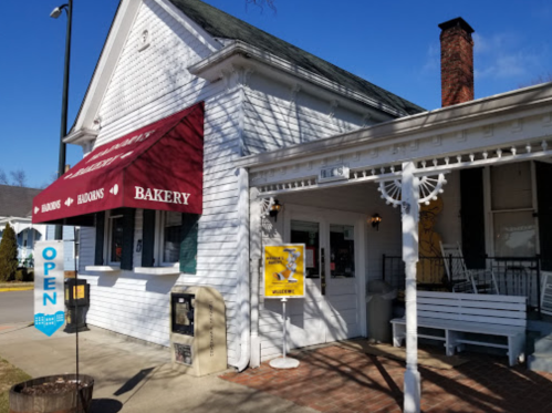 A charming white bakery building with a red awning, open sign, and a welcoming porch.