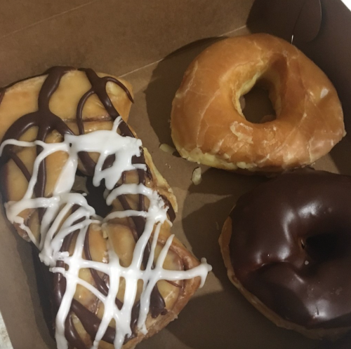 A box containing three donuts: one glazed, one chocolate frosted, and one with chocolate and white icing drizzles.