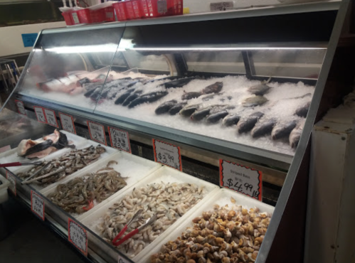 A seafood display case filled with various fish and shellfish on ice, with price tags visible.