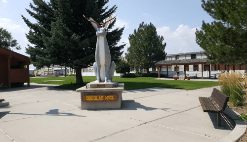 A large statue of a jackrabbit stands in a park with trees and benches, featuring a sign that reads "DOUGLAS WYO."