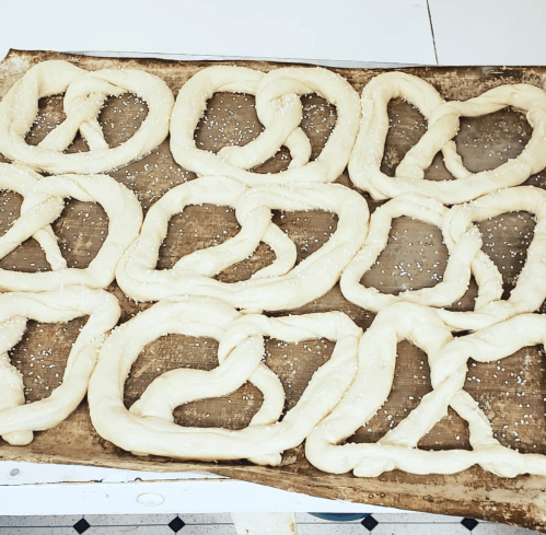 A baking sheet with uncooked pretzel dough shaped into various pretzel forms, sprinkled with coarse salt.