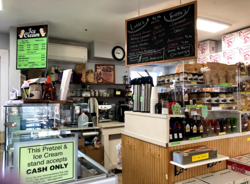 A cozy ice cream shop interior with a menu board, coffee machines, and a cash-only sign at the counter.