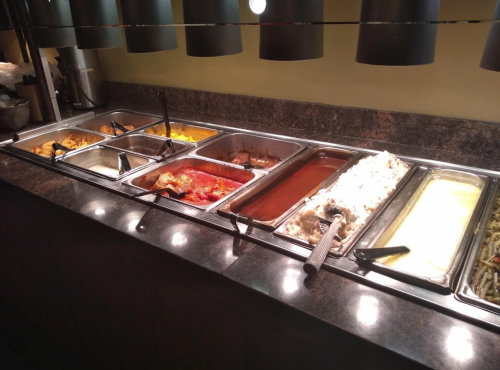 A buffet line featuring various dishes in metal trays, including rice, vegetables, and sauces under warmers.
