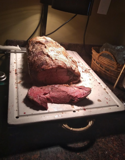 A large roast beef on a cutting board, with a slice cut off, under warm kitchen lighting.