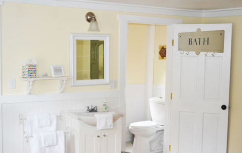 Bright bathroom with yellow walls, a mirror, sink, towels, and a door labeled "BATH."