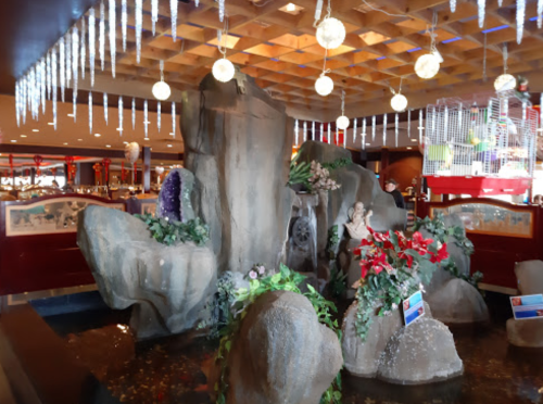A decorative indoor rock formation with plants and flowers, featuring a small water feature and hanging lights above.
