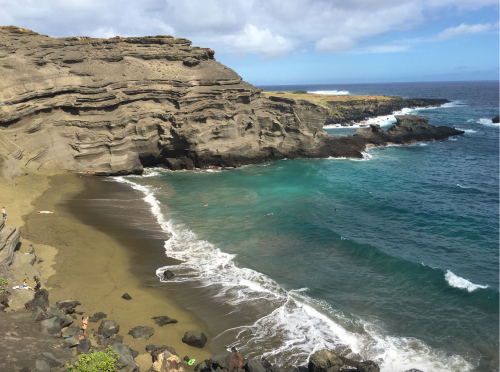 A scenic view of a rocky coastline with turquoise waters and gentle waves lapping at a sandy beach.
