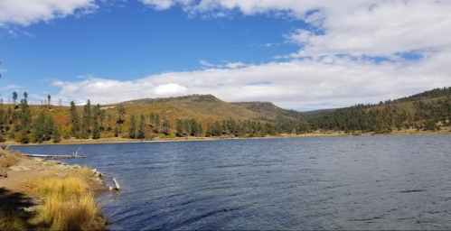 A serene lake surrounded by trees and hills under a partly cloudy sky.
