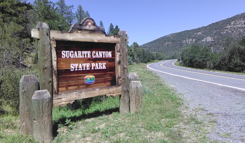 Sign for Sugarite Canyon State Park beside a winding road, surrounded by greenery and mountains in the background.