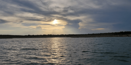 A serene lake at sunset, with soft clouds and a golden sun reflecting on the water's surface.