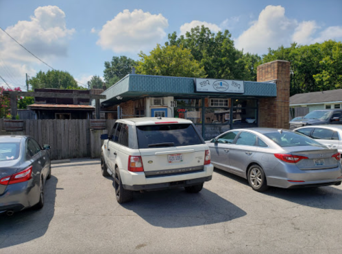 A parking lot with several cars in front of a BBQ restaurant under a blue sky with scattered clouds.