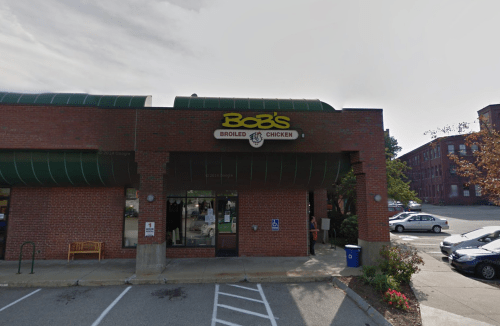 Exterior of Bob's Broiled Chicken restaurant, featuring a brick facade and green awning, with parked cars nearby.