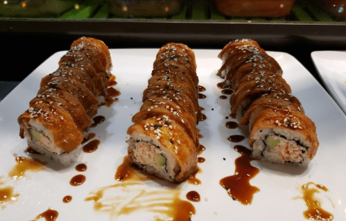 Three sushi rolls drizzled with sauce and sprinkled with sesame seeds, served on a white plate.