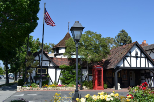 A charming Tudor-style building with an American flag, a red telephone booth, and colorful flowers in the foreground.