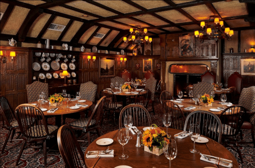 Cozy dining room with wooden beams, elegant tables, floral centerpieces, and warm lighting.