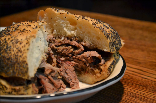 A close-up of a poppy seed bun filled with tender, shredded beef on a wooden table.