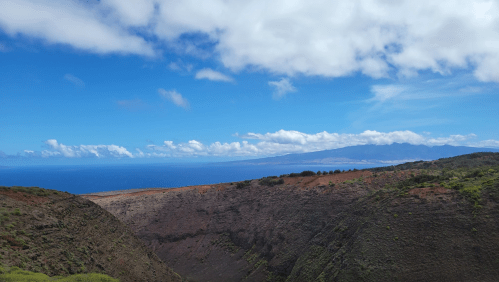 A panoramic view of a volcanic crater with lush greenery and a blue ocean under a partly cloudy sky.