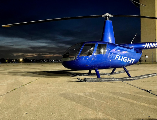 A blue helicopter parked on a concrete surface at dusk, with a cloudy sky in the background.