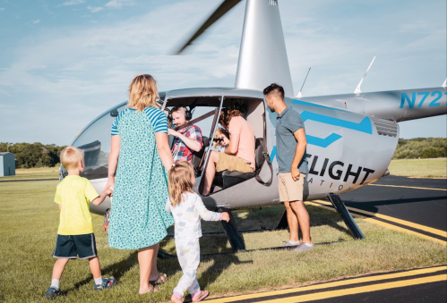 A family approaches a helicopter on a sunny day, with children excitedly leading the way.