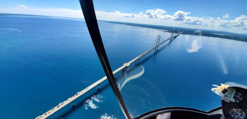 Aerial view of a long bridge spanning a blue body of water under a clear sky with scattered clouds.