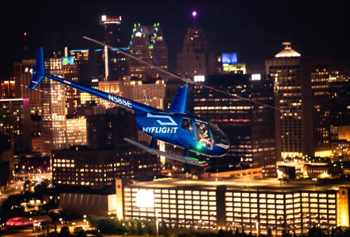 A helicopter flying over a city skyline at night, illuminated by city lights.