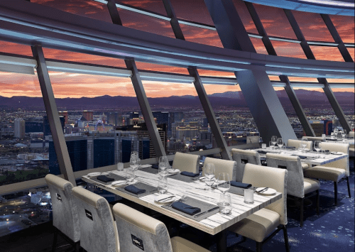 Elegant restaurant interior with panoramic windows showcasing a sunset view over a city skyline.