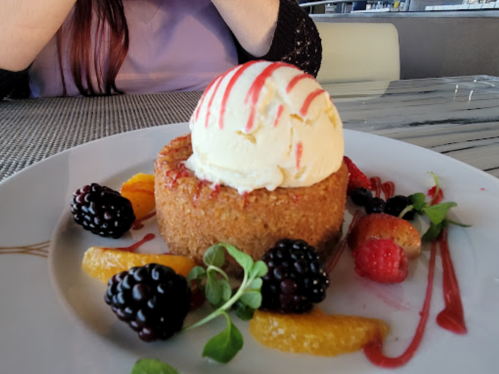 A dessert plate featuring a round cake topped with ice cream, surrounded by berries and orange slices.