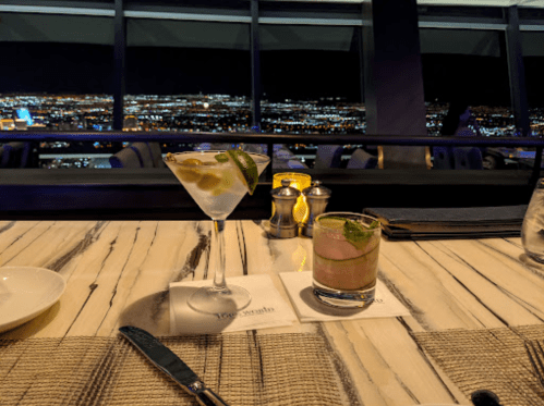 Two cocktails on a table with a stunning city view at night, illuminated by soft candlelight.