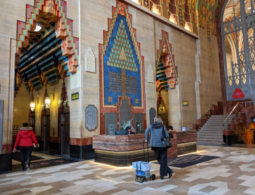 Interior of a grand lobby with colorful geometric designs, a reception area, and visitors walking through.