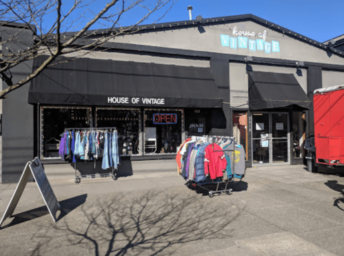 A vintage clothing store with an "OPEN" sign, featuring racks of clothes outside and a red truck nearby.