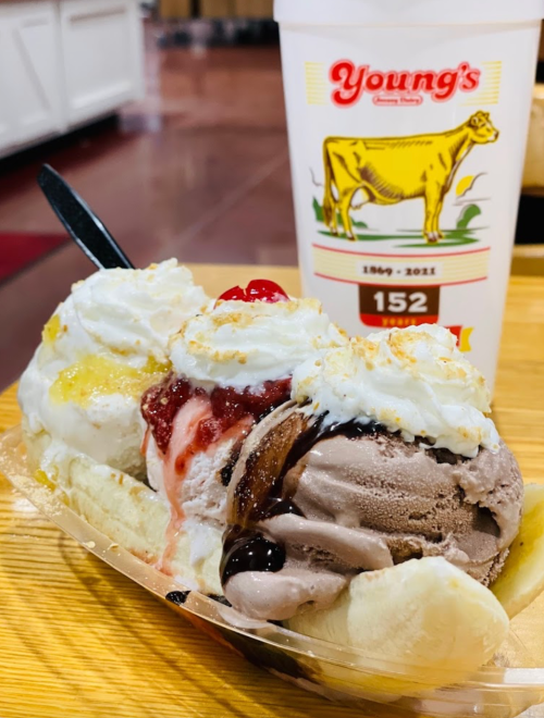 A banana split with three scoops of ice cream, topped with whipped cream, cherries, and chocolate sauce, next to a drink.