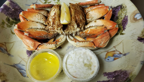 A plate with a cooked crab, lemon wedge, and two dipping sauces: one yellow and one white with bits of vegetables.