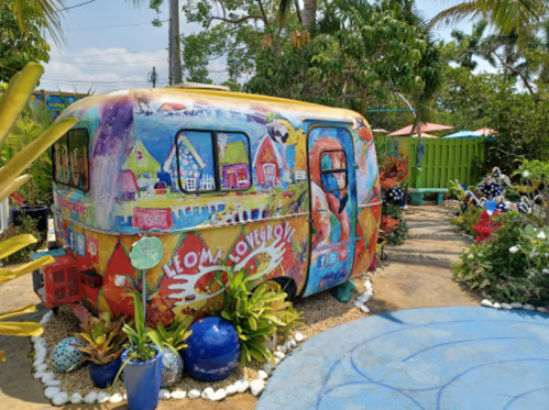 Colorful, artistic trailer surrounded by vibrant plants and a blue circular patio in a sunny garden setting.