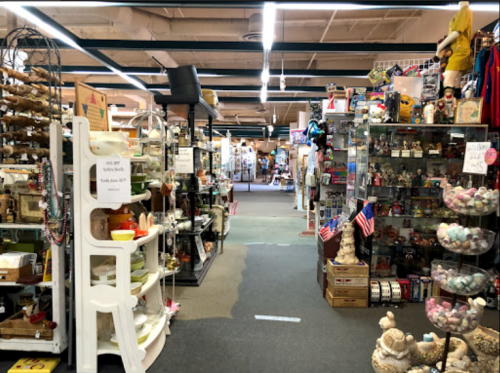 A wide aisle in a vintage shop filled with various collectibles, displays, and decorations on both sides.