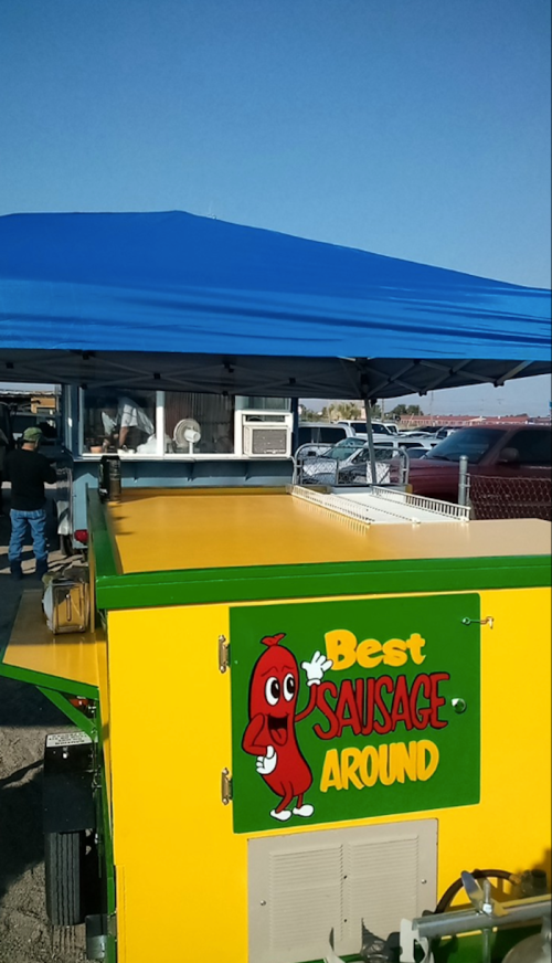 A colorful food cart with a blue canopy, featuring a sign that reads "Best Sausage Around" with a cartoon sausage character.