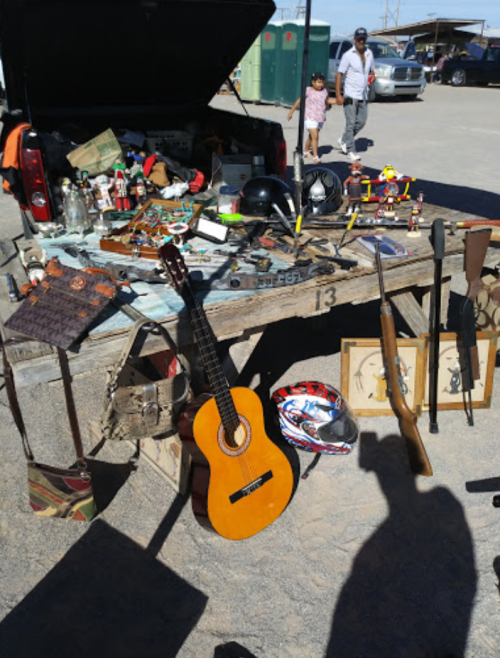 A table filled with various vintage items, including a guitar, helmets, tools, and framed pictures, at a market.
