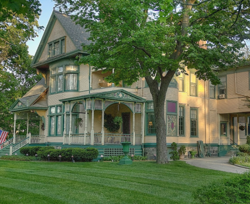 A large, elegant Victorian-style house surrounded by lush greenery and a well-maintained lawn.