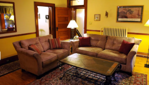 Cozy living room with a beige sofa set, a coffee table, and warm lighting, featuring wooden accents and a patterned rug.
