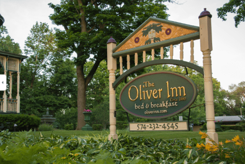 Sign for The Oliver Inn bed and breakfast, surrounded by greenery, with a phone number and website displayed.