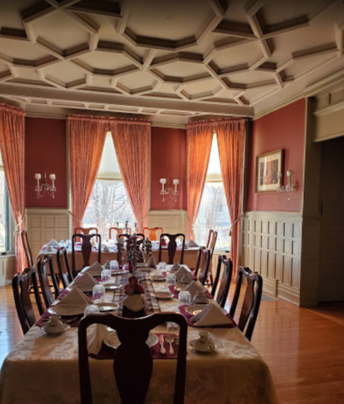 Elegant dining room with a long table set for a meal, featuring ornate ceiling and large windows with drapes.